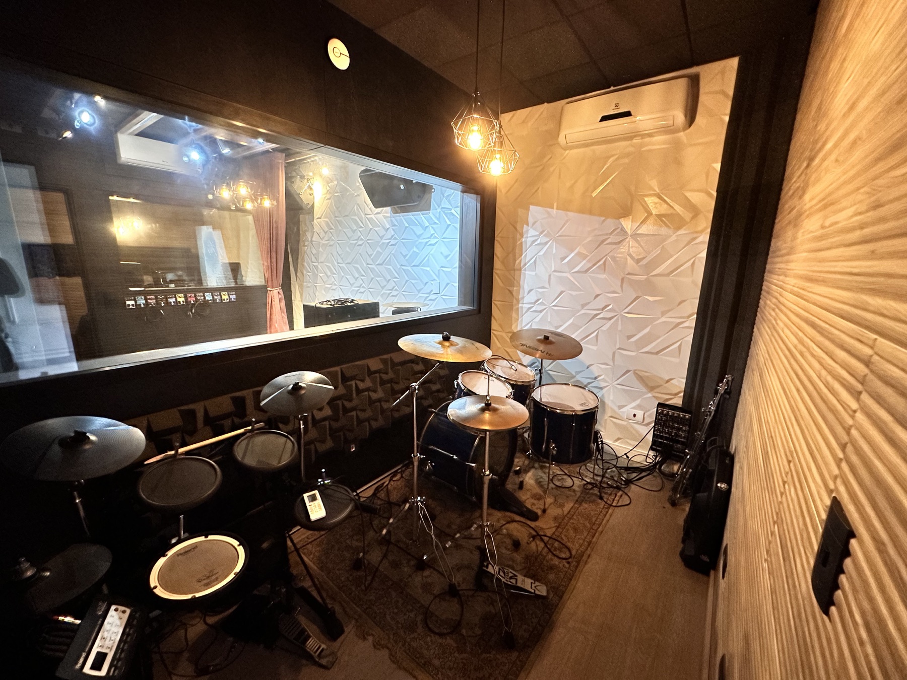 Sala de gravação com bateria acústica, bateria eletrônica e visor de vidro para a cabine técnica